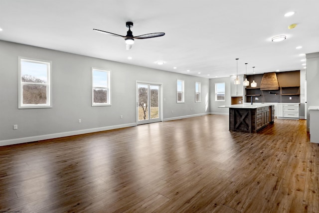 unfurnished living room with dark wood-style floors, recessed lighting, a ceiling fan, a sink, and baseboards