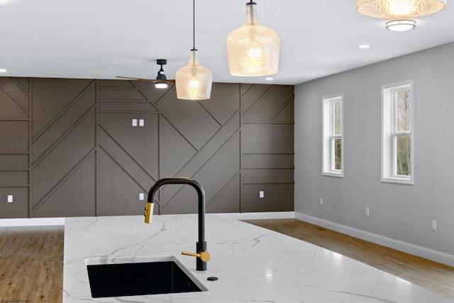 kitchen with baseboards, light stone counters, a sink, and pendant lighting