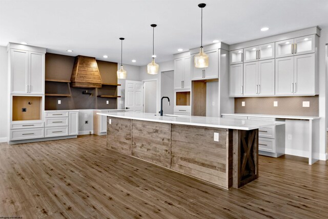 kitchen with dark wood-style floors, a sink, a large island with sink, and decorative backsplash