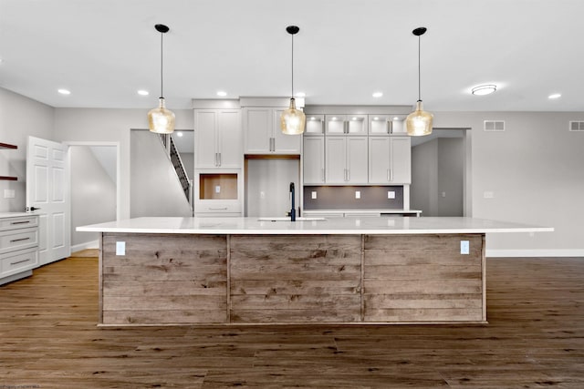 kitchen featuring visible vents, wood finished floors, a large island with sink, white cabinetry, and a sink