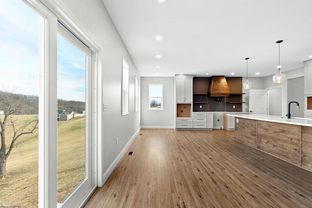 kitchen with baseboards, light wood-style flooring, hanging light fixtures, a sink, and recessed lighting