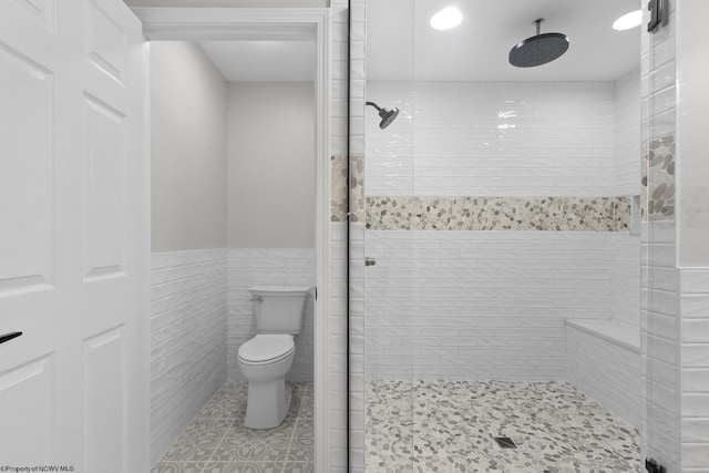 bathroom with a wainscoted wall, tile walls, toilet, a stall shower, and tile patterned flooring