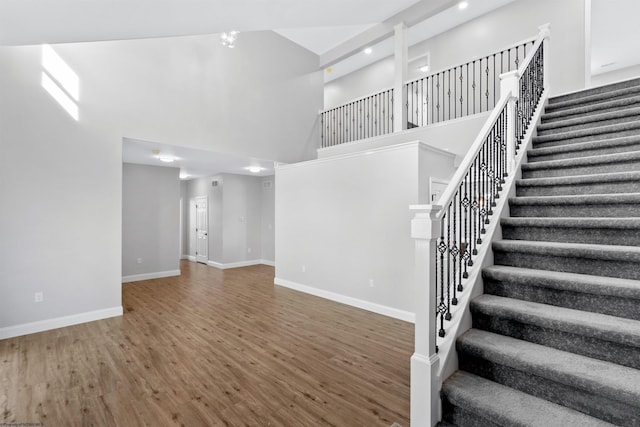 interior space featuring a towering ceiling, stairs, baseboards, and wood finished floors