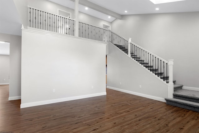 interior space with a skylight, wood finished floors, high vaulted ceiling, baseboards, and stairs