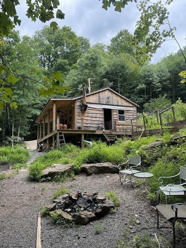 rear view of house with an outdoor fire pit, a wooden deck, and a view of trees