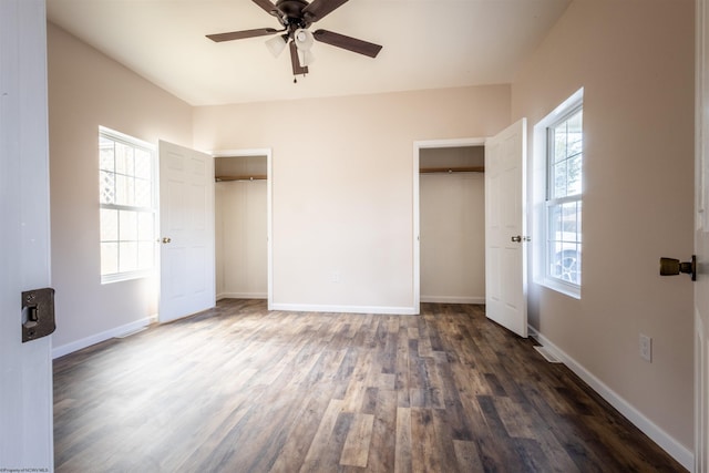 unfurnished bedroom featuring multiple closets, dark wood finished floors, baseboards, and ceiling fan