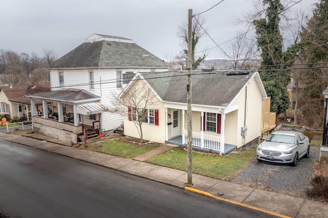 view of front of property featuring covered porch, a shingled roof, and a front lawn