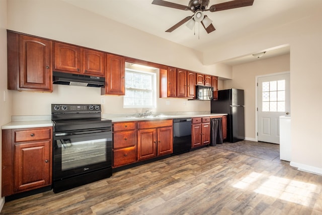 kitchen featuring wood finished floors, under cabinet range hood, light countertops, black appliances, and a sink