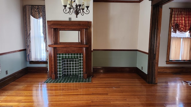 unfurnished living room featuring an inviting chandelier, baseboards, a tiled fireplace, and wood finished floors