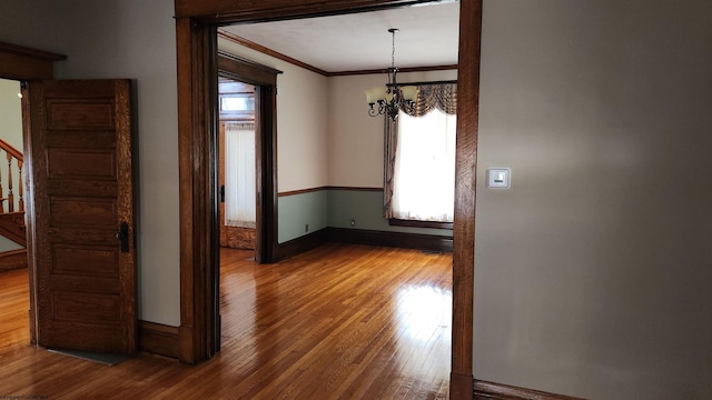 unfurnished dining area featuring baseboards, hardwood / wood-style flooring, ornamental molding, stairs, and a chandelier