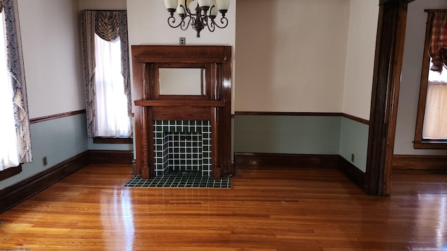 unfurnished living room with baseboards, a notable chandelier, a tiled fireplace, and wood finished floors