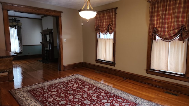 unfurnished dining area featuring wood-type flooring, visible vents, and baseboards