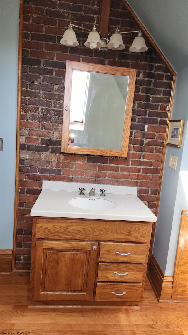 bathroom with brick wall, baseboards, wood finished floors, and vanity