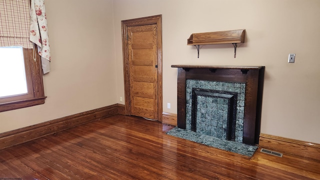 unfurnished living room with a tiled fireplace, wood-type flooring, visible vents, and baseboards