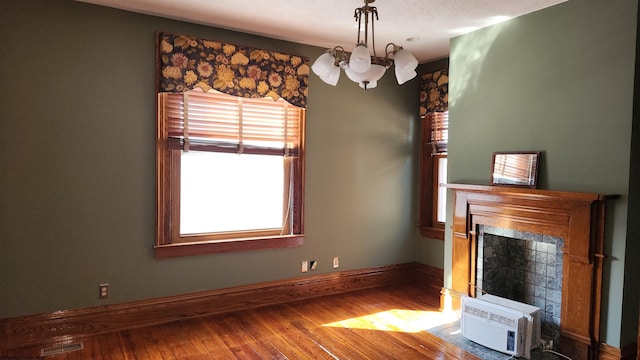 unfurnished living room featuring a fireplace, wood-type flooring, visible vents, an inviting chandelier, and a wall mounted air conditioner