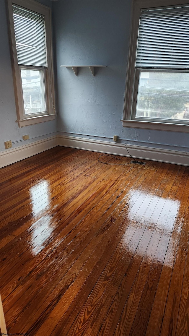 empty room featuring a healthy amount of sunlight, baseboards, and hardwood / wood-style floors