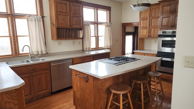 kitchen featuring a kitchen breakfast bar, a center island, light countertops, stainless steel appliances, and a sink