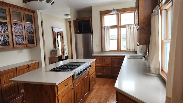 kitchen featuring glass insert cabinets, appliances with stainless steel finishes, brown cabinets, and light countertops