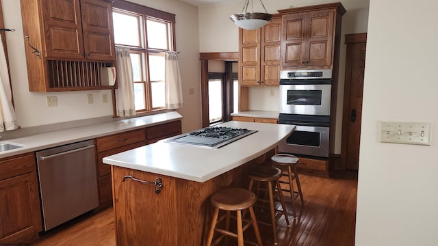 kitchen with a kitchen island, a breakfast bar, wood finished floors, stainless steel appliances, and light countertops