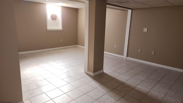 finished basement featuring a paneled ceiling, light tile patterned floors, and baseboards