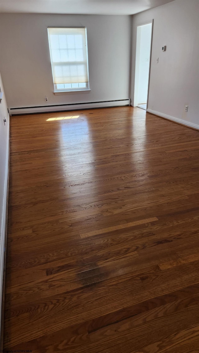 empty room with baseboards, a baseboard heating unit, and dark wood finished floors