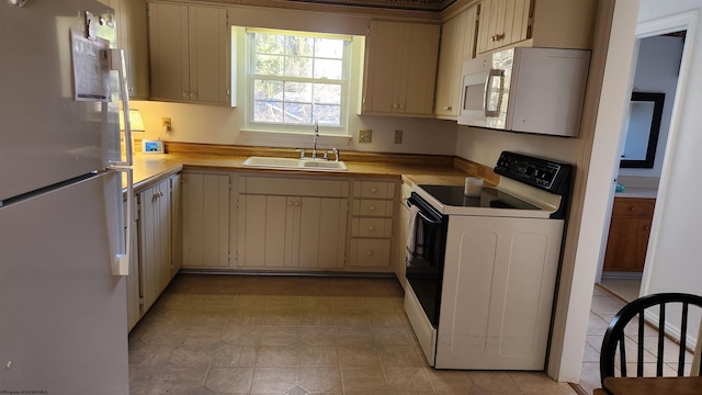 kitchen with white appliances, cream cabinetry, light countertops, and a sink