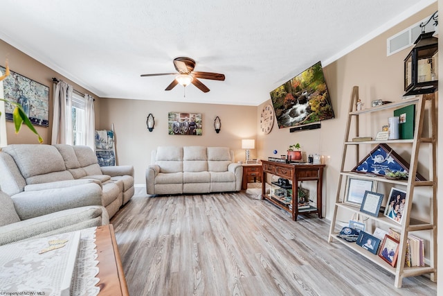 living room featuring ceiling fan, a textured ceiling, wood finished floors, visible vents, and ornamental molding