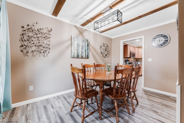 dining space featuring light wood finished floors, baseboards, and a textured ceiling