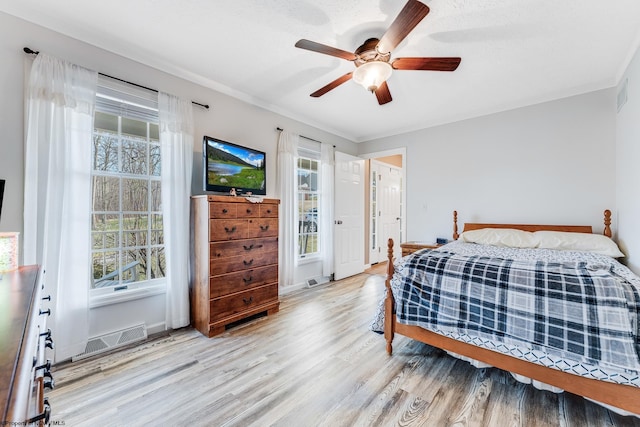 bedroom featuring a ceiling fan, multiple windows, visible vents, and wood finished floors