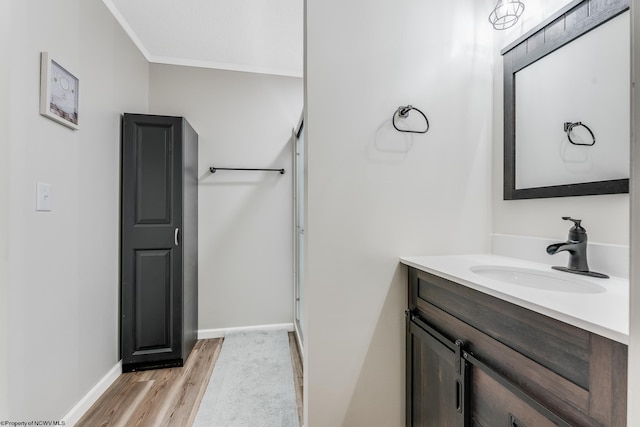 bathroom featuring wood finished floors, vanity, baseboards, ornamental molding, and an enclosed shower