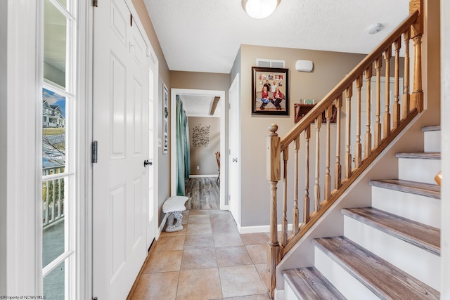 entryway featuring a textured ceiling, light tile patterned floors, visible vents, and baseboards