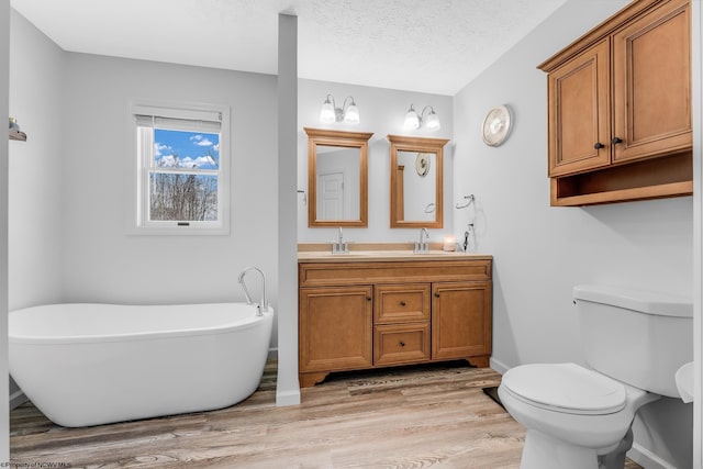 full bathroom with double vanity, toilet, wood finished floors, a textured ceiling, and a freestanding tub