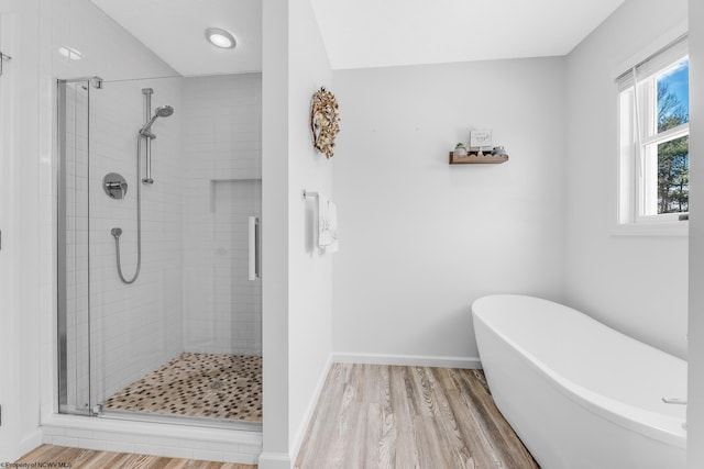 full bathroom featuring a freestanding tub, a shower stall, baseboards, and wood finished floors