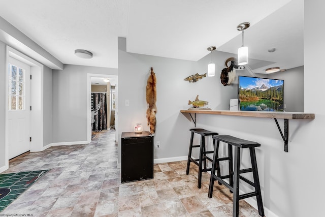 kitchen with a breakfast bar, stone finish floor, decorative light fixtures, and baseboards