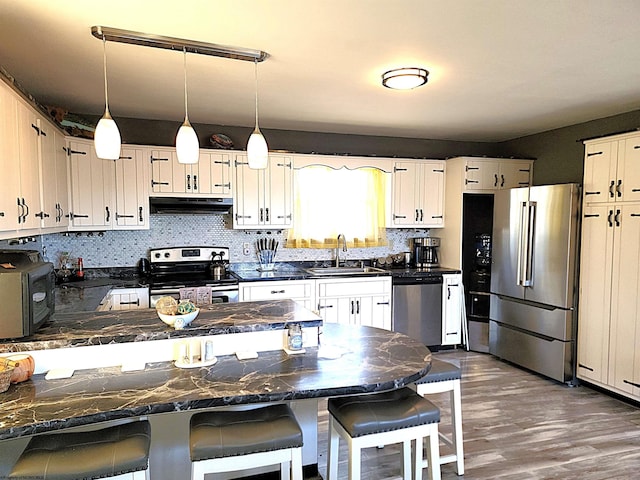 kitchen featuring dark countertops, a peninsula, stainless steel appliances, under cabinet range hood, and a sink