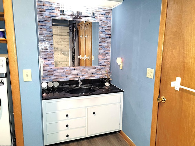 bathroom featuring tasteful backsplash, stacked washer / drying machine, vanity, wood finished floors, and baseboards