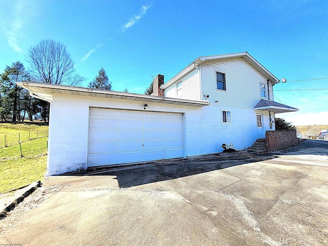 view of side of property with concrete driveway, fence, a chimney, and an attached garage