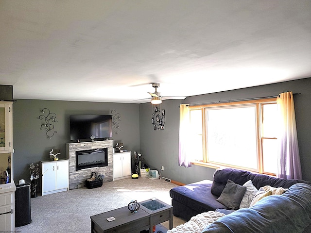 carpeted living area featuring a glass covered fireplace, a ceiling fan, and baseboards