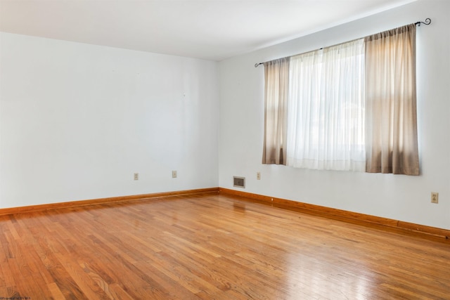 empty room featuring baseboards, visible vents, and hardwood / wood-style floors