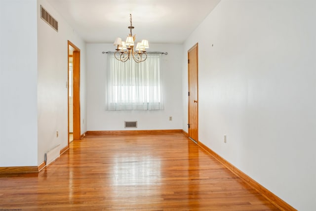 spare room featuring an inviting chandelier, visible vents, and wood finished floors