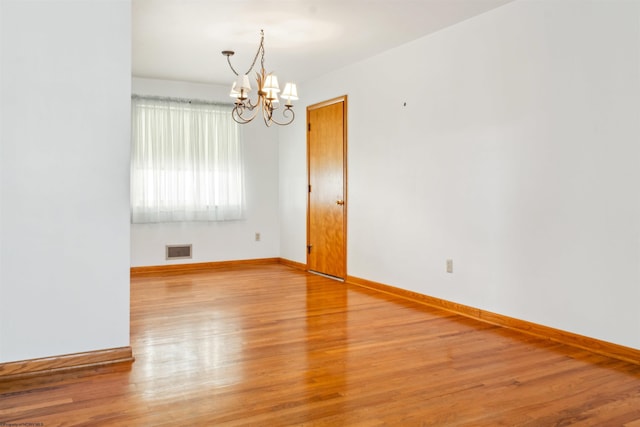 spare room featuring baseboards, wood finished floors, visible vents, and an inviting chandelier