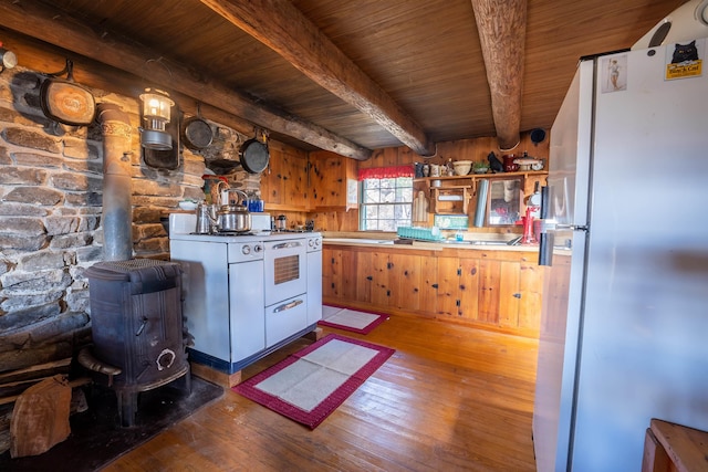 kitchen with white appliances, wood ceiling, hardwood / wood-style floors, beamed ceiling, and a wood stove