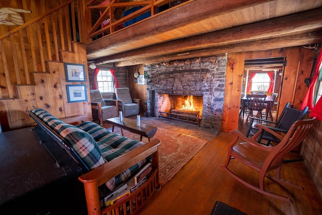 living room with hardwood / wood-style floors, wood walls, beam ceiling, and a stone fireplace