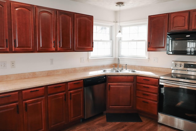 kitchen with appliances with stainless steel finishes, reddish brown cabinets, light countertops, and a sink