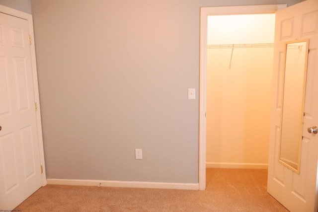 unfurnished bedroom with a closet, light carpet, a spacious closet, and baseboards