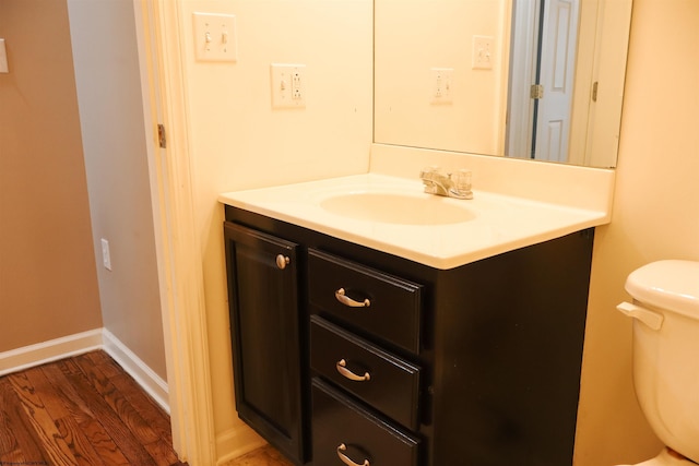 half bathroom featuring toilet, baseboards, wood finished floors, and vanity