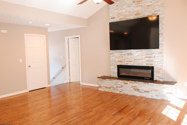 unfurnished living room featuring lofted ceiling, ceiling fan, a stone fireplace, and wood finished floors