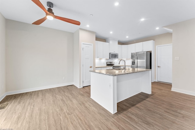 kitchen featuring light stone counters, a kitchen island with sink, white cabinetry, appliances with stainless steel finishes, and light wood-type flooring