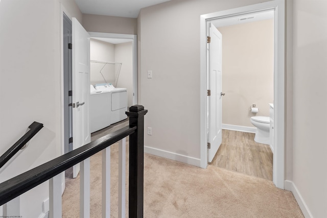 hallway featuring visible vents, washing machine and dryer, carpet flooring, an upstairs landing, and baseboards