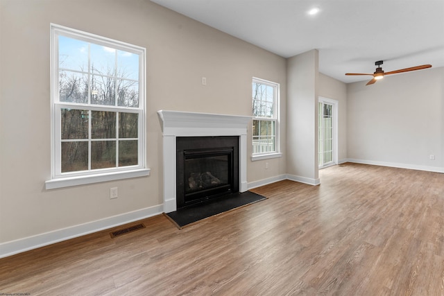 unfurnished living room featuring baseboards, visible vents, wood finished floors, and a glass covered fireplace